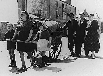A photo of a refugee family walking with a cart